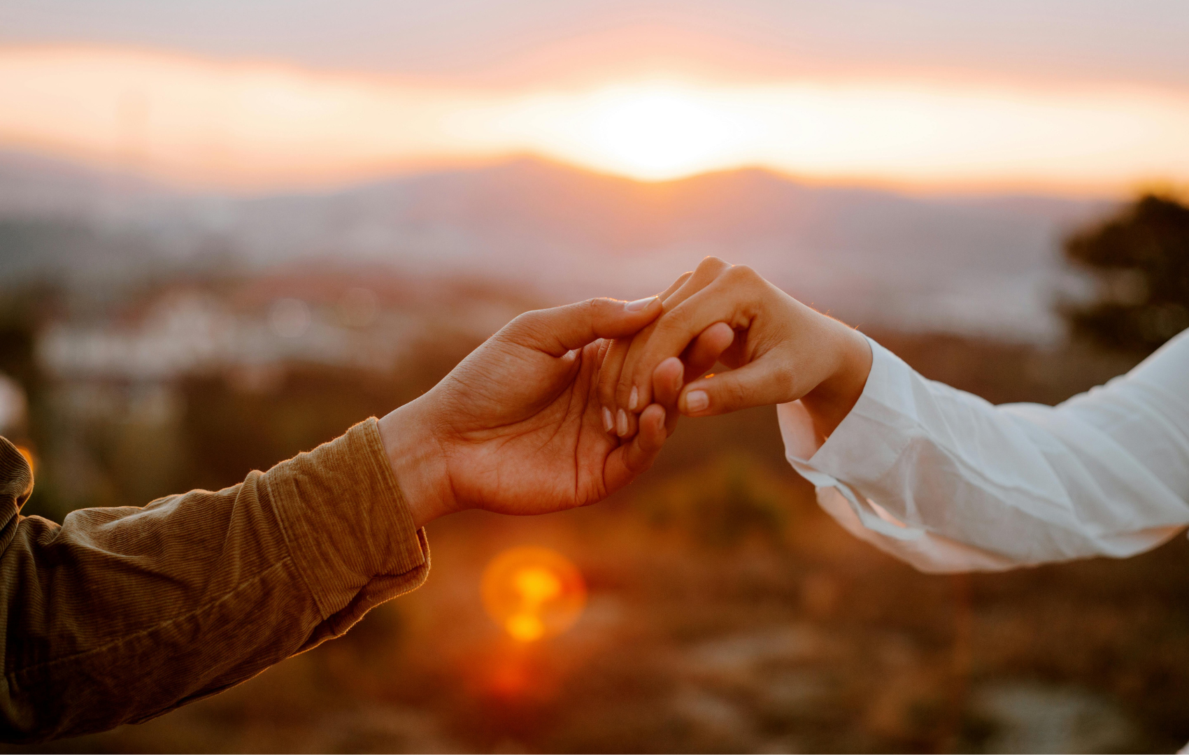 Two hands reaching toward each other at sunset